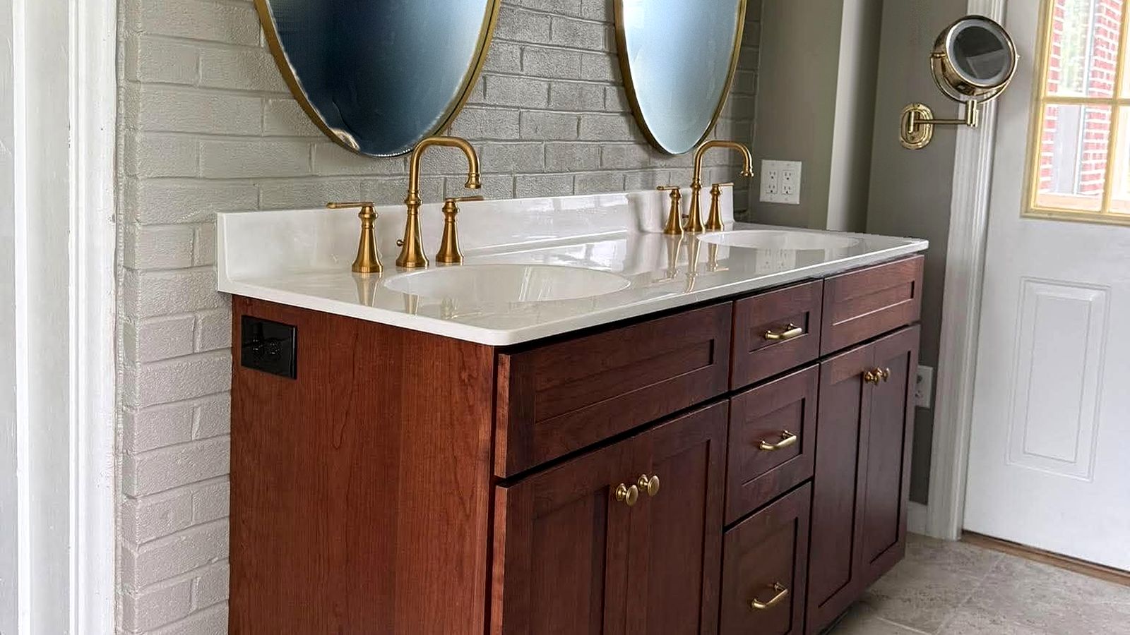Walnut double vanity with brass faucets and oval mirrors